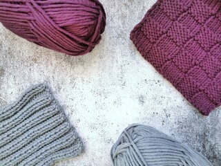 Pieces of purple and gray knitting and skeins of yarn on gray background top view. Knitted patterns and textures close up. Handmade and needlework hobbies. 