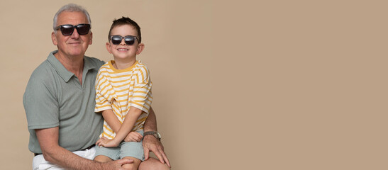 Grandfather with his grandson are posing in photo studio in modern clothes on brown background.