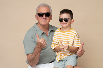 Grandfather with his grandson are posing in photo studio in modern clothes on brown background.