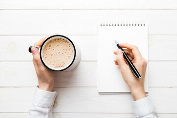 Woman hand with pencil writing on notebook and hold coffee cup. Woman working on office table with coffee