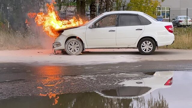 Accident. A white car in an industrial area is on fire. The engine compartment is on fire