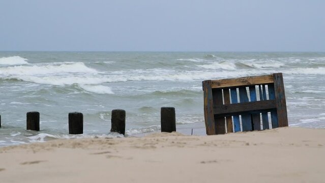 Old blue wooden EPAL palette on the shore, trash and waste litter on an empty Baltic sea white sand beach, environmental pollution problem, overcast day, distant medium shot