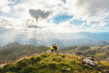 Fototapeta premium Couple of hikers with backpacks, standing and embracing on the top of a mountain contemplating the landscape of the mountain range. sports and outdoor activities.