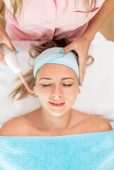 Fototapeta na wymiar Beautician therapist applying face treatment in beauty salon to young woman.