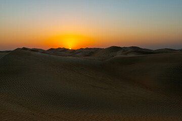 stunning and beautiful sunset over there wide and amazing desert with the sub setting over the dunes in the horizon
