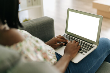 Young african woman working on laptop computer at home sitting on sofa.