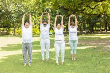 Group of indian senior people wearing white dress doing stretching exercise outdoor at summer park. Fitness concept.