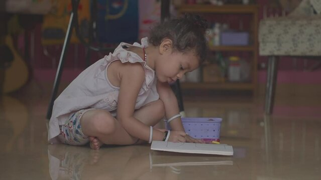 A pretty little girl sitting on a living room floor drawing and colouring in pictures in her colouring book at home indoors 