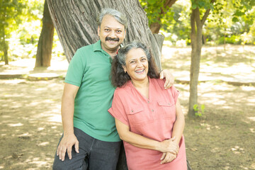 Happy indian senior couple standing together at summer park.