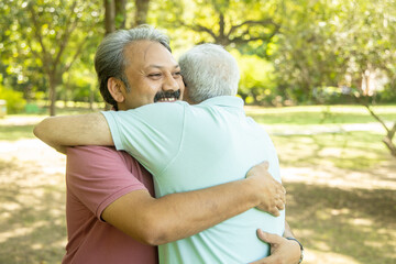 Naklejka na ściany i meble Happy senior indian men hugging each other, Mature aged old friends meeting and greeting outdoor at summer park.