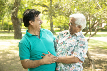 Happy senior indian men hugging each other, Mature aged old friends meeting and greeting outdoor at summer park.
