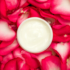 Cosmetic cream container, top view, rose petals background.