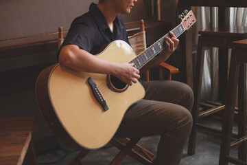 A close up of musician playing an acoustic guitar for entertainment or practicing for perfomance. Concept of indoor activity, lifestyle and leisure. A guitarist is focusing and enjoy playing guitar. 