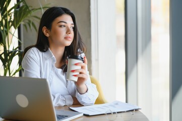 Young charming female freelancer using laptop computer for distance job while sitting in modern coffee shop interior, beautiful Caucasian woman working on net-book during morning breakfast in cafe bar