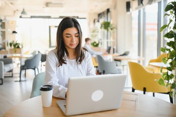 Smiling girl student study online with skype teacher, happy young woman learn language listen lecture watch webinar write notes look at laptop sit in cafe, distant education