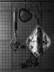 Old italian vintage kitchen utensils. Potholder, strainer and whisk hanging on racks on kitchen wall.