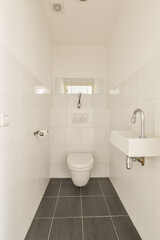 Modern toilet installed on white wall under button and illuminated shelf in light restroom at home