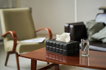 Close-up of tissues in box and glass of water preparing for psychotherapy on table at office of...