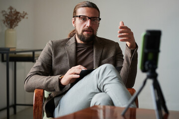 Bearded mature therapist having online consultation with patient sitting in front of smartphone on...