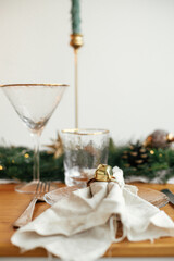 Stylish Christmas table setting. Linen napkin with bell on plate, vintage cutlery, wineglass, fir branches with golden lights, pine cones and candle on table. Atmospheric Holiday brunch