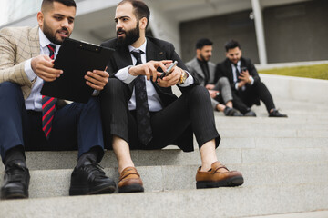 Business people outdoor meeting. Several men in suits sit on the steps of a street staircase during a work break. Successful promotion and recognition in the team of employees.