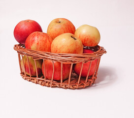 Red ripe apples in a wicker basket on a white background.