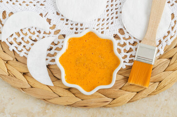 Orange fruit mask (scrub) in a small white bowl, cosmetic brush and cotton pads. Homemade face or...