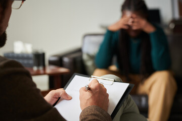 Close-up of psychologist making notes in document while talking to patient during session