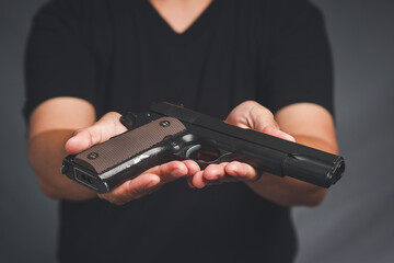 Hand holding a gun while standing on a gray background - obrazy, fototapety, plakaty