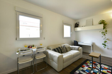 living room with white leather sofa, small folding table with breakfast served with juice and fruits and colorful carpet on the floor
