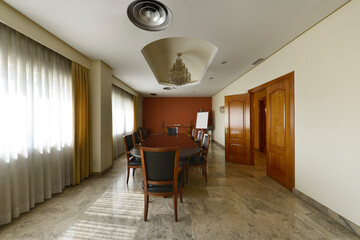 Boardroom of a conventional office with a long wooden table with matching chairs with black leather upholstered seats and marble floors