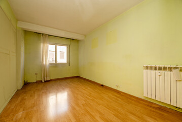 Empty living room with parquet floor, bay window with aluminum window, aluminum radiator and pistachio green walls