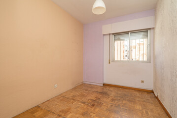 Empty living room with old parquet floor, walls painted in different colors and window with bars