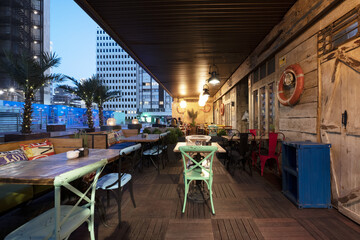 Dining room on the terrace of a bar with wooden floors and disparate tables