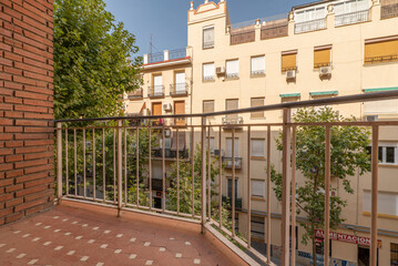 View of a street from a balcony with young trees, balconies with plants and skies with clouds and clear