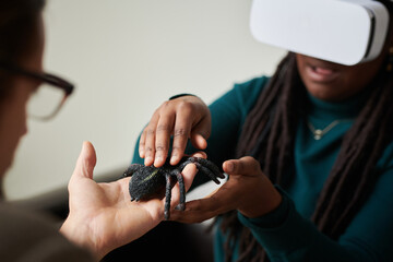 Fototapeta na wymiar African American girl in VR glasses touching artificial spider during virtual therapy with therapist