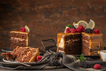 Delicious semi-naked chocolate cake with caramel topping and decorated with blackberries and raspberries. Dark background