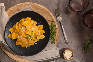 Farfalle pasta with pumpkin sauce and parmesan cheese decorated with rosemary on a black ceramic...