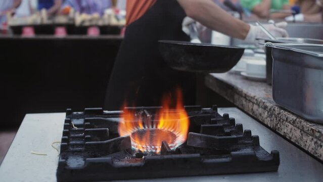 Chef cooking with fire in a frying pan at a street food festival. Professional Flambe style kitchen.