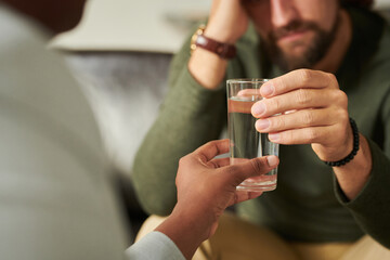 Close-up of depressed patient drinking water giving by psychologist during consultation at office