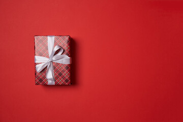 Red gift box with white ribbon on red background.