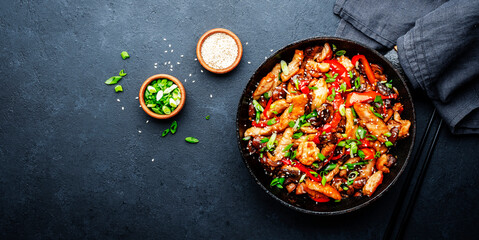 Stir fry with turkey fillet, paprika, mushrooms, green chives and sesame seeds in frying pan. Asian cuisine dish. Black stone kitchen table background, top view