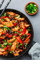 Stir fry with chicken, red paprika, mushrooms and chives in frying pan. Asian cuisine dish. Gray kitchen table background, top view, copy space
