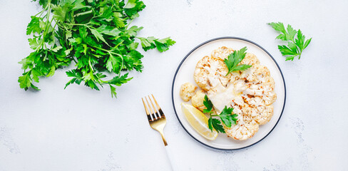 Baked cauliflower steak on plate, white table background, top view