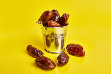 A small metal bucket filled with dried dates on a yellow background.