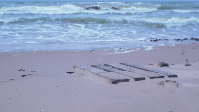 Old wooden EPAL palette covered with sand, trash and waste litter on an empty Baltic sea white sand beach, environmental pollution problem, overcast day, medium shot