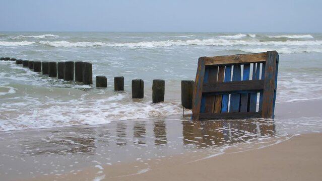 Old blue wooden EPAL palette on the shore, trash and waste litter on an empty Baltic sea white sand beach, old wooden pier, environmental pollution problem, overcast day, medium shot