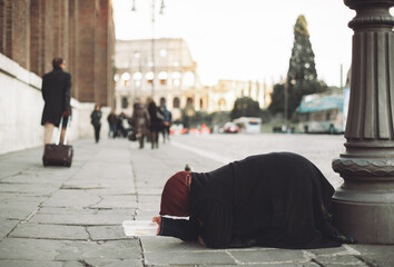 a woman on her knees begs for alms on a city street.