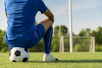 Athlete standing with ball on football field during sunrise, soccer ball in net on sky background, ball movement, popular sports on football club.