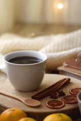 Cup of tea or coffee, various spices, bowl of cookies, tangerines, books, reading glasses and knitted blanket on wooden table. Hygge at home concept, selective focus.